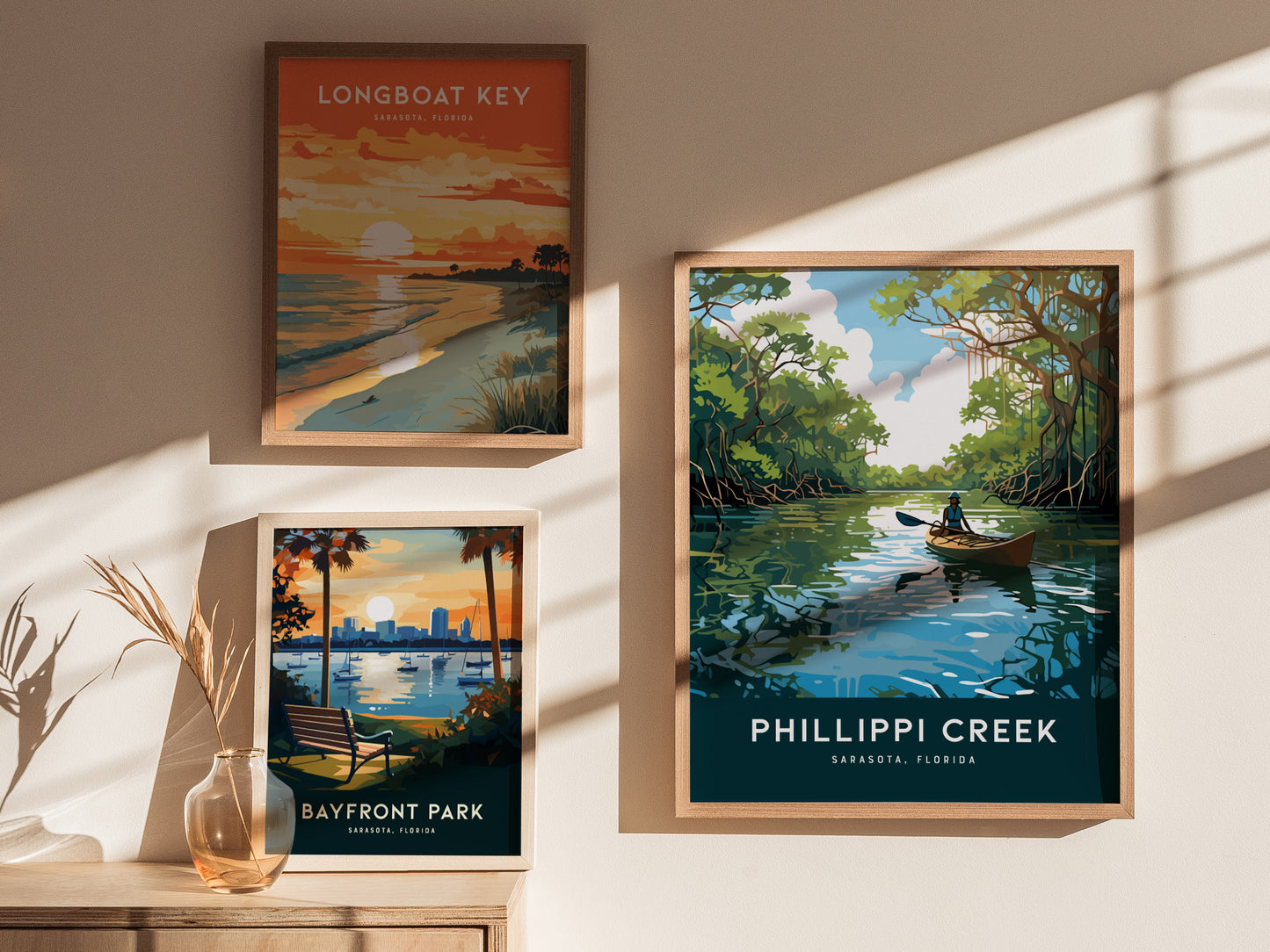 Three framed posters on a wall depict scenic Florida locations: Longboat Key at sunset, Bayfront Park with a city skyline, and Phillippi Creek with a kayaker on a calm waterway.