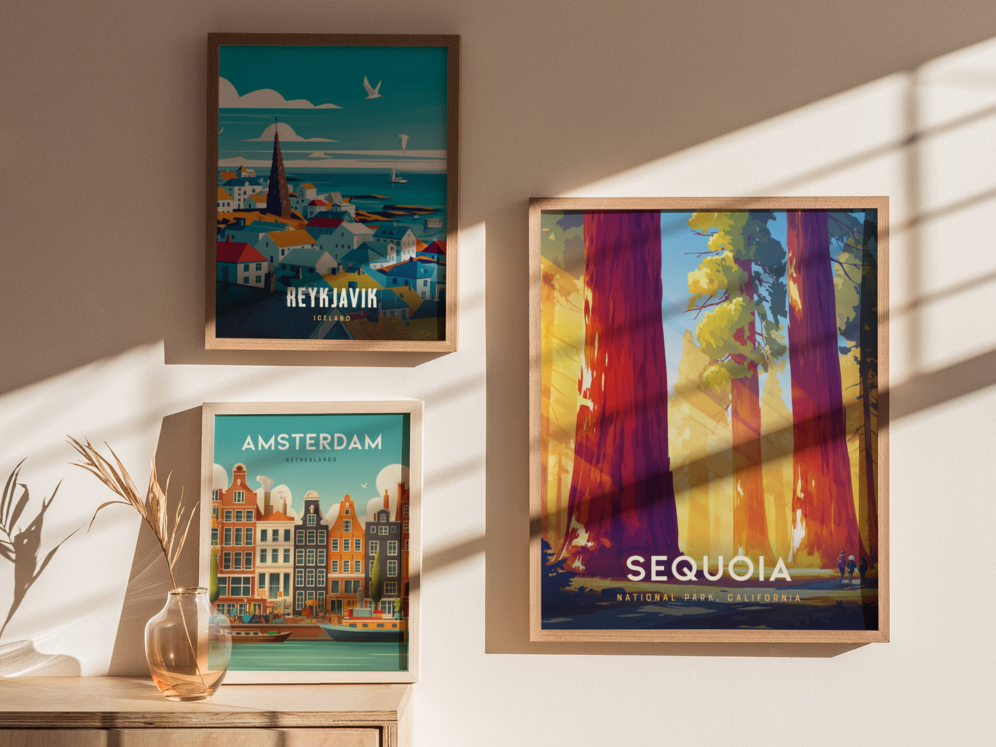 Three framed posters on a sunlit wall depict Reykjavik, Amsterdam, and Sequoia National Park, showcasing vibrant cityscapes and towering trees. A small vase with dried plants sits below.