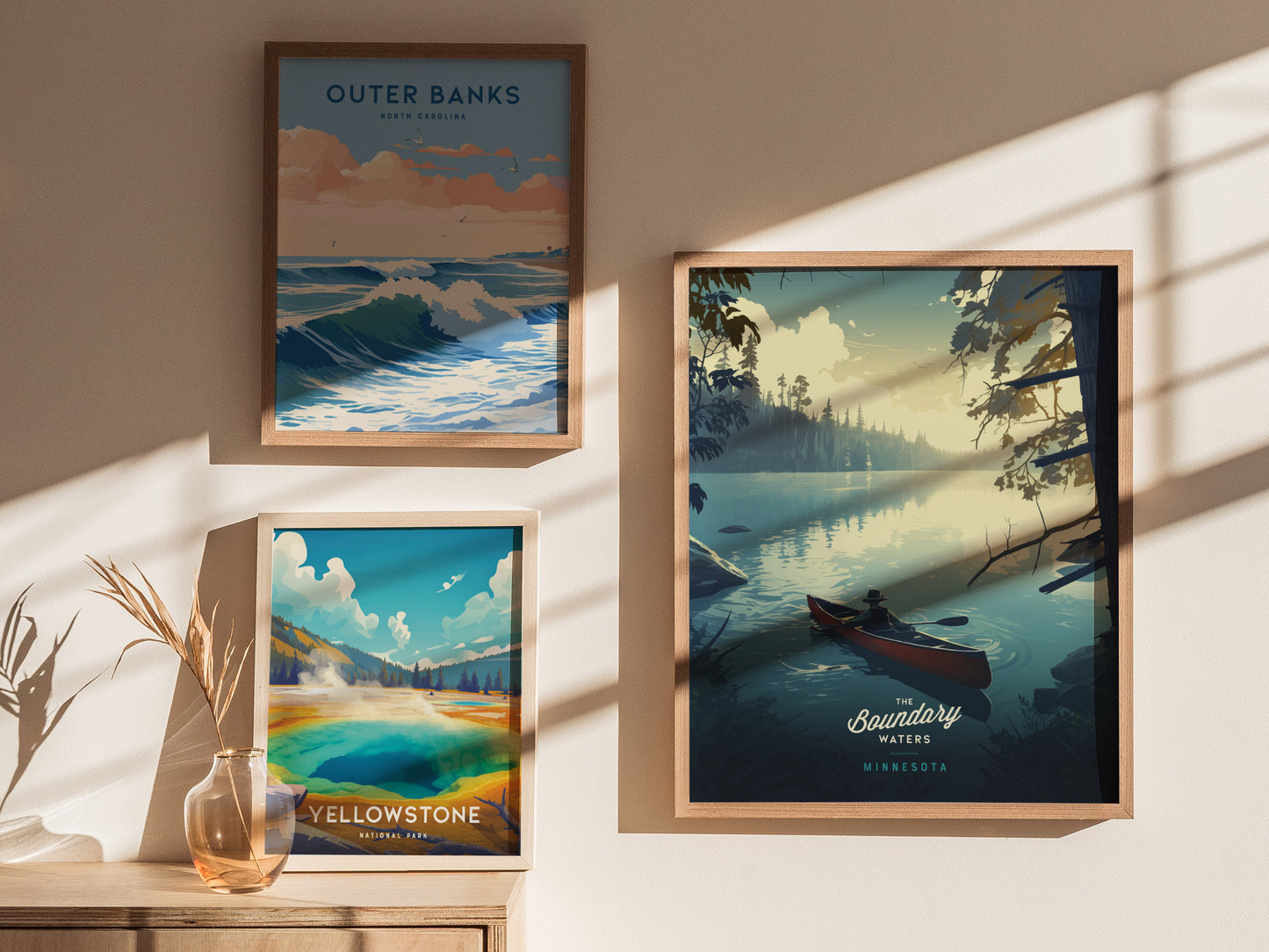 Three framed posters are displayed on a sunlit wall, featuring scenic landscapes of Outer Banks, Yellowstone, and Boundary Waters with a canoeist on a tranquil lake.