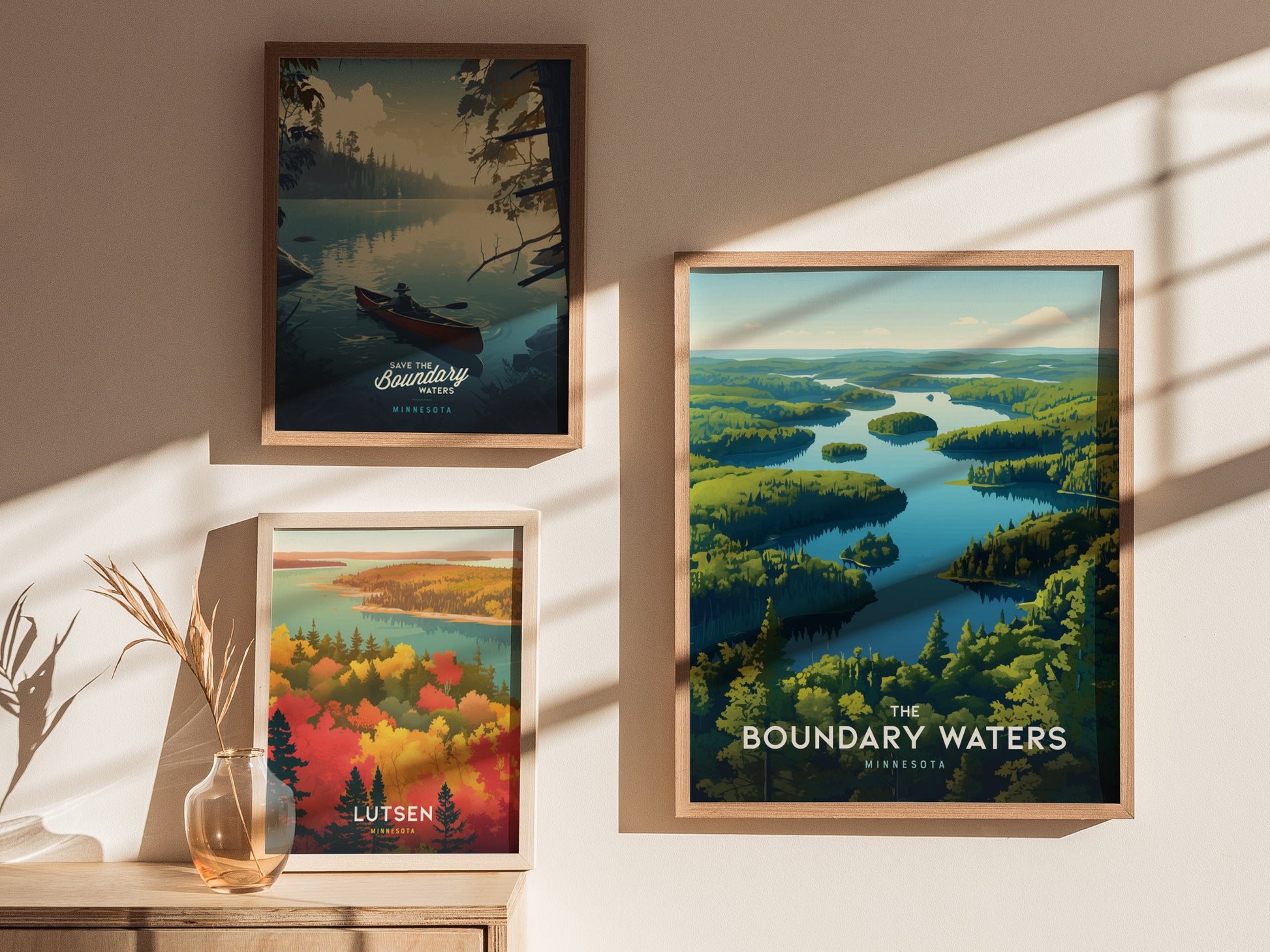 Three framed posters on a wall depict serene wilderness scenes with lakes and forests, each highlighting Minnesota locations. Sunlight casts soft shadows, creating a warm and inviting atmosphere.