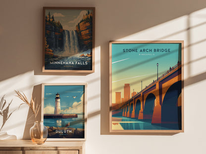 Three framed posters are displayed on a wall, featuring Stone Arch Bridge, Minnehaha Falls, and a lighthouse in Duluth. Sunlight casts soft shadows across the arrangement.