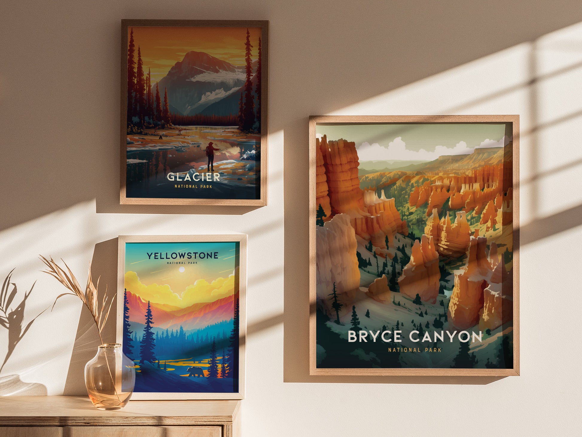 Three framed national park prints are displayed on a wall, featuring Bryce Canyon, Glacier, and Yellowstone. Sunlight casts shadows across the artwork and a wooden surface below.