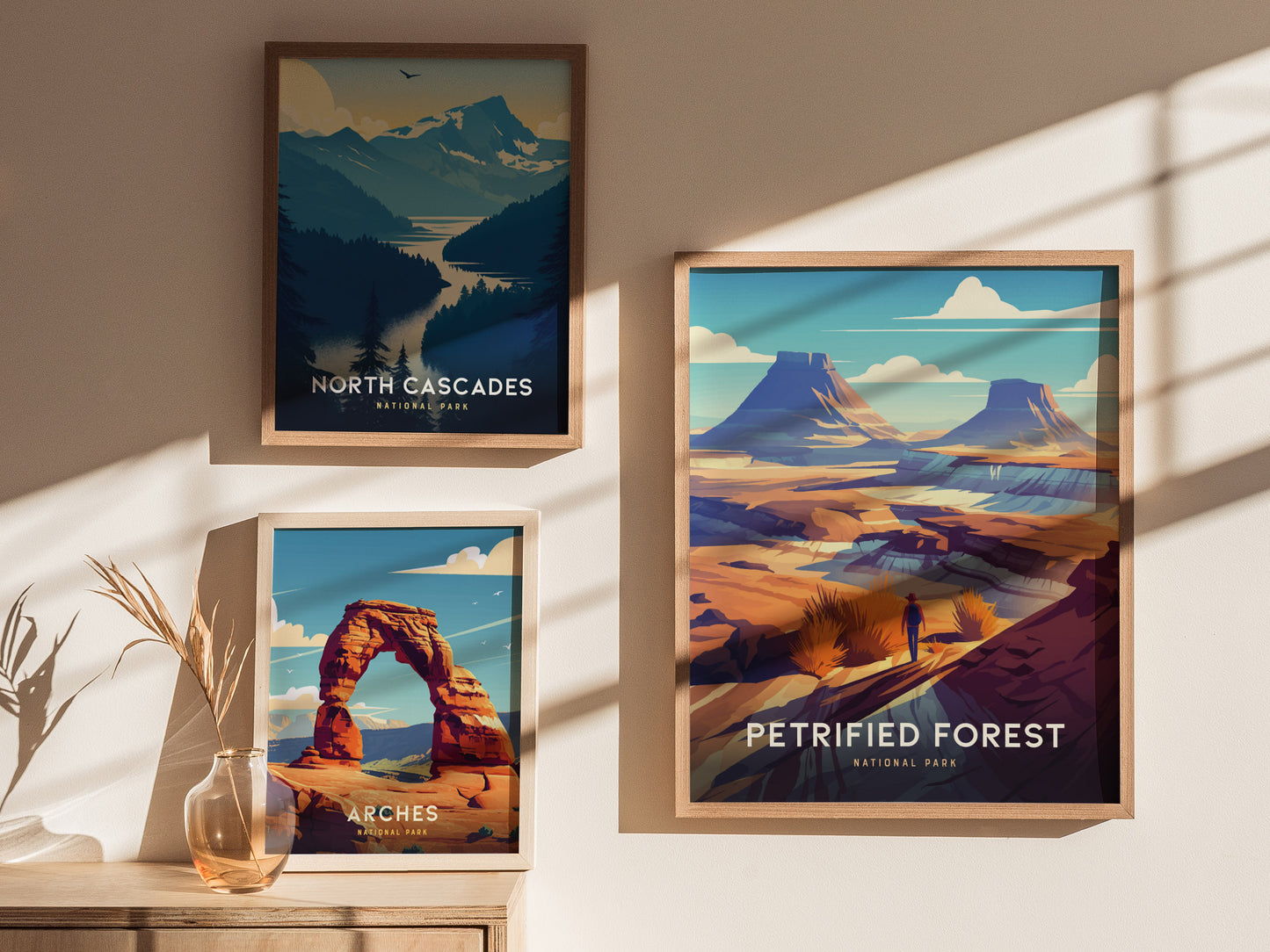 Three framed posters on a wall display art of North Cascades, Arches, and Petrified Forest National Parks, each with vibrant landscapes and natural features. Sunlight casts shadows across the scene.