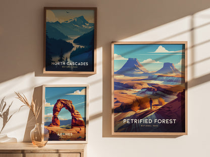 Three framed posters on a wall display art of North Cascades, Arches, and Petrified Forest National Parks, each with vibrant landscapes and natural features. Sunlight casts shadows across the scene.