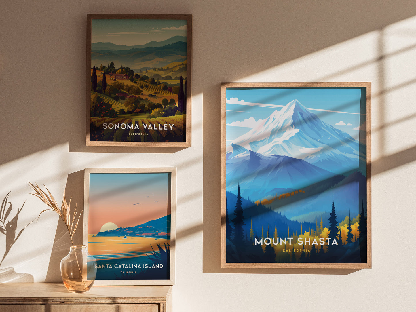 Three framed posters are displayed on a sunlit wall, featuring Mount Shasta, Sonoma Valley, and Santa Catalina Island, each with vibrant colors and scenic landscapes.