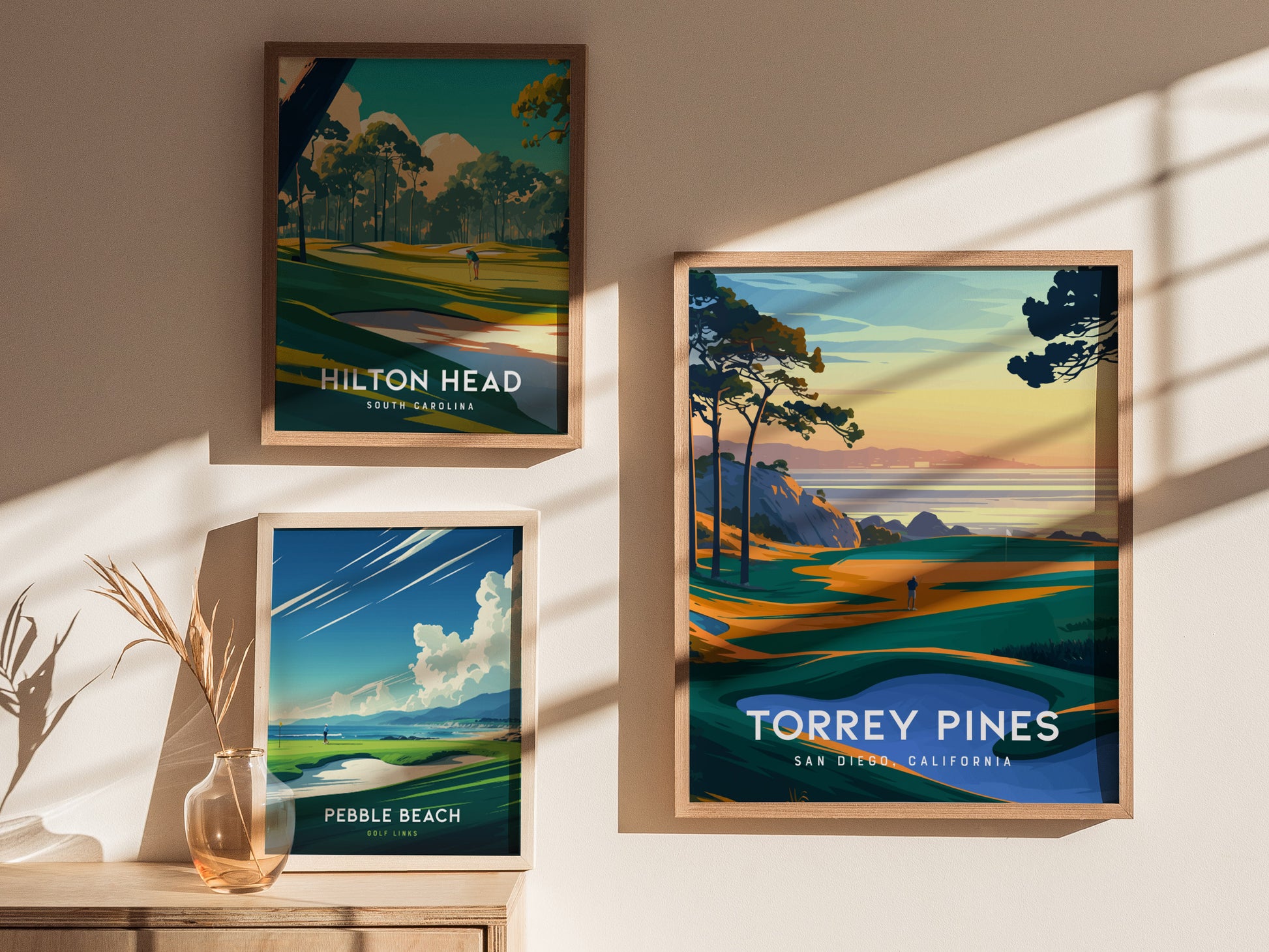 Three framed posters on a sunlit wall depict golf courses: Torrey Pines with coastal cliffs, Hilton Head in a forested area, and Pebble Beach with an ocean view.