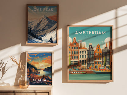 Three framed posters hang on a wall, depicting Lone Peak, Acadia National Park, and Amsterdams iconic canals with colorful buildings. Soft sunlight casts shadows across the artwork.