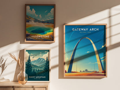 Three framed posters are displayed on a wall: Gateway Arch, Yellowstone, and Rocky Mountain, with sunlight casting shadows and a decorative vase with dried plants nearby.