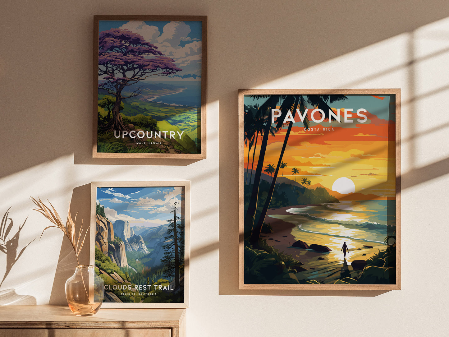 Framed posters on a wall feature a sunset over Pavones, Costa Rica, a vibrant landscape in Upcountry Maui, Hawaii, and Clouds Rest Trail in Yosemite, California, with decorative shadows.