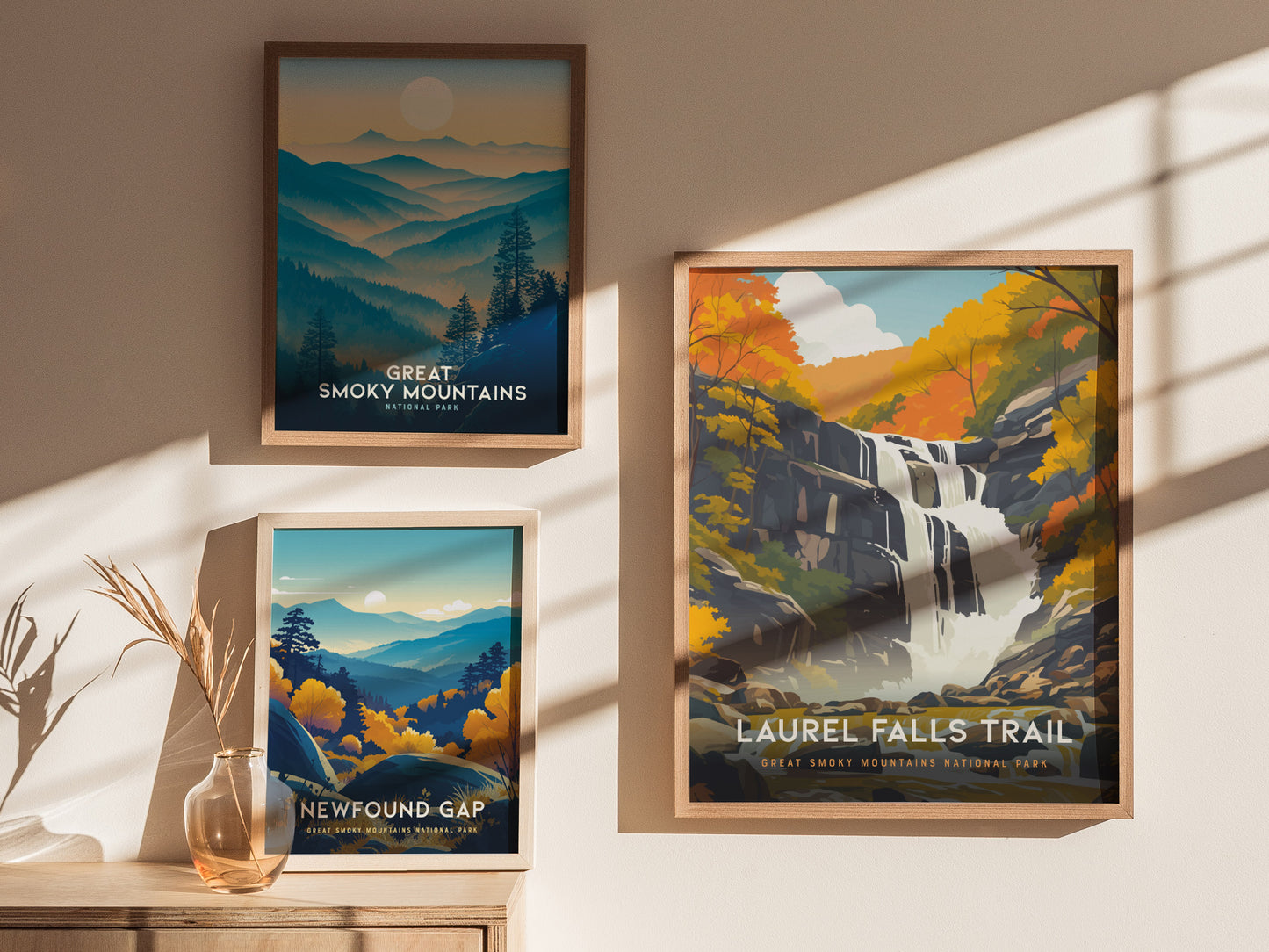 Three framed posters are displayed on a sunlit wall, featuring artistic landscapes of the Great Smoky Mountains, including a waterfall, mountain ranges, and colorful autumn foliage.
