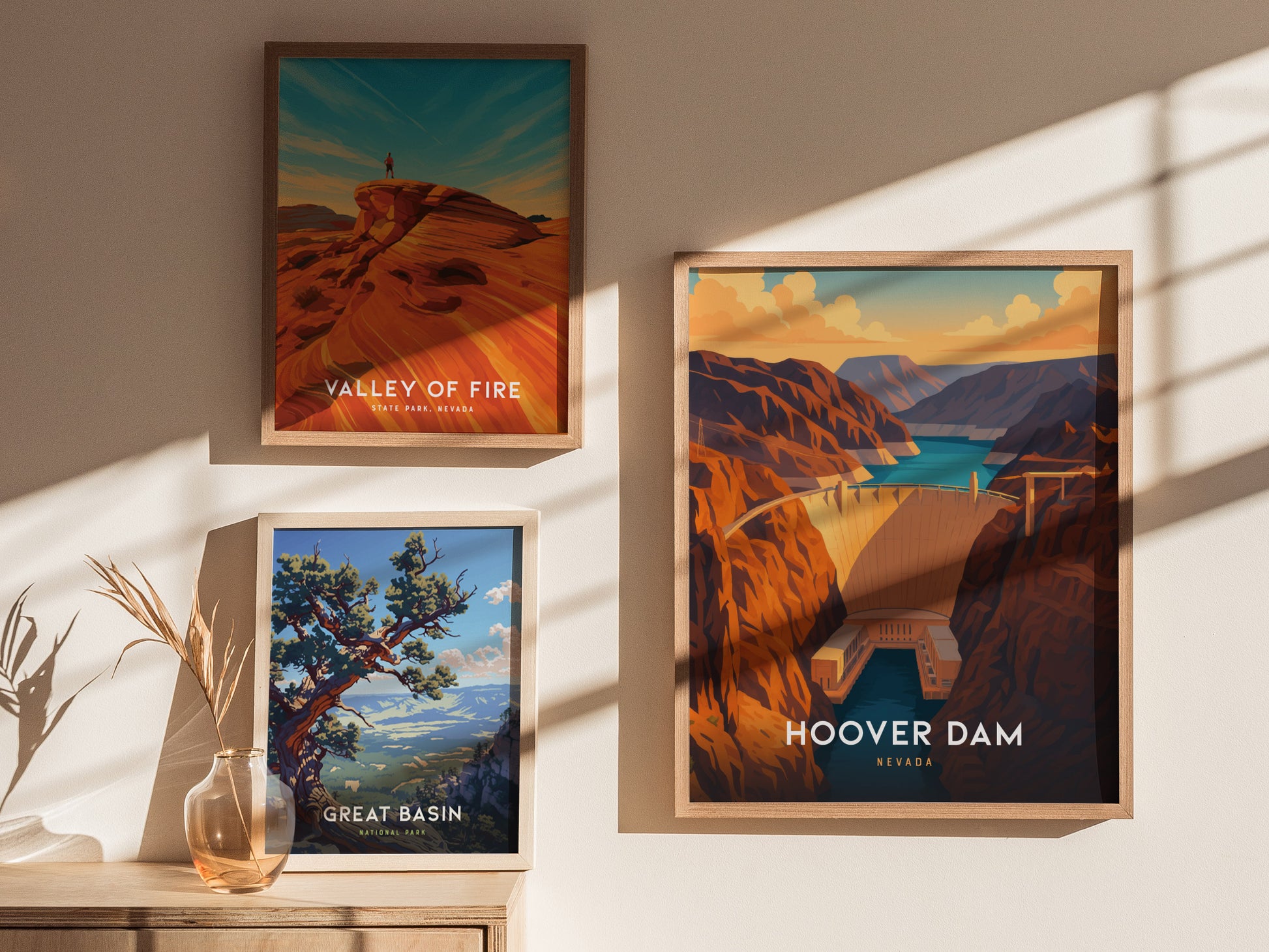 Three framed travel posters are displayed on a wall. The posters depict the Valley of Fire, Great Basin, and Hoover Dam, each with vibrant illustrations showcasing natural landscapes. Sunlight casts shadows across the wall.