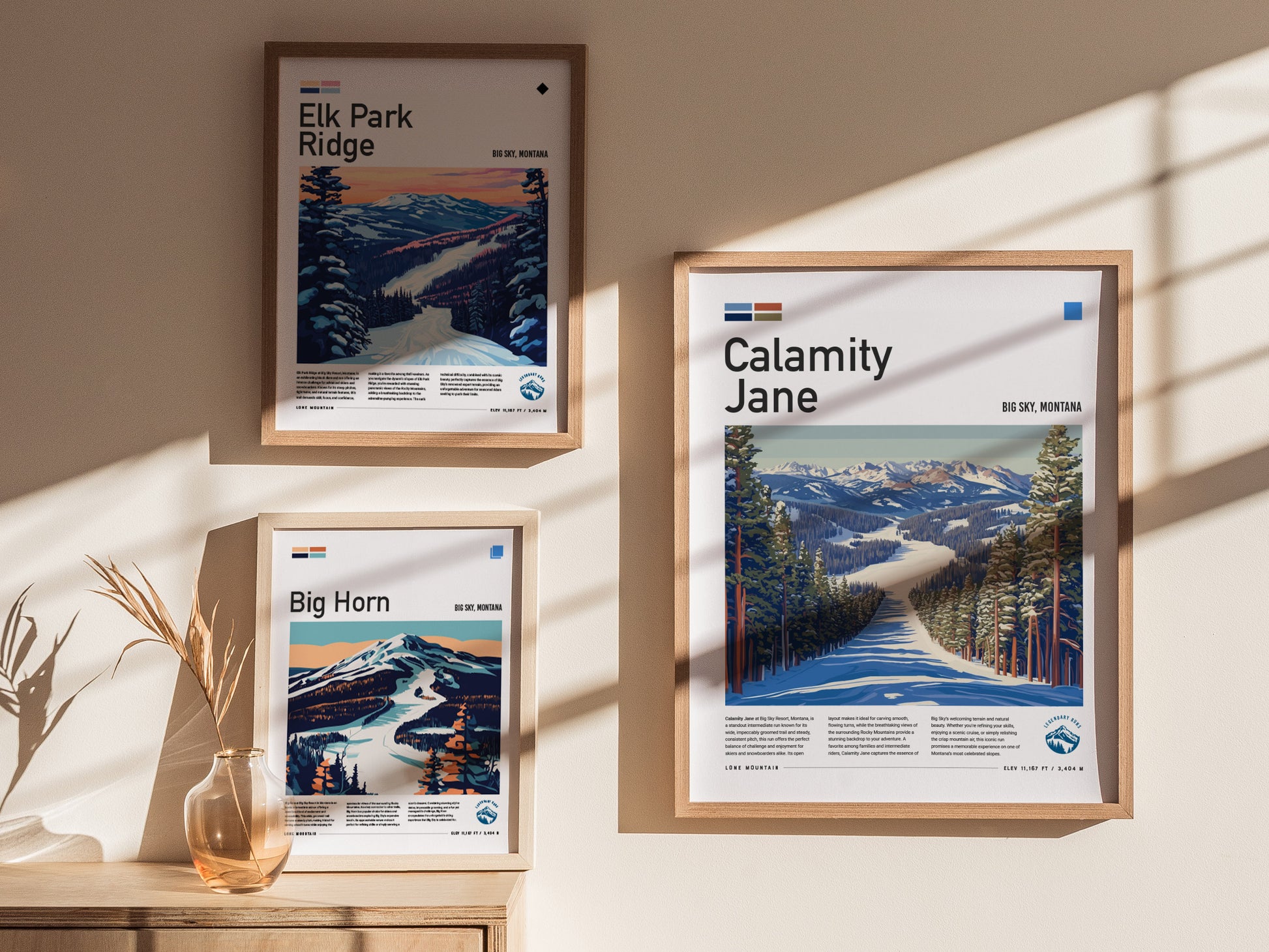 Three framed posters on a sunlit wall depict ski runs at Big Sky, Montana, including Calamity Jane, Elk Park Ridge, and Big Horn, with scenic mountain landscapes.