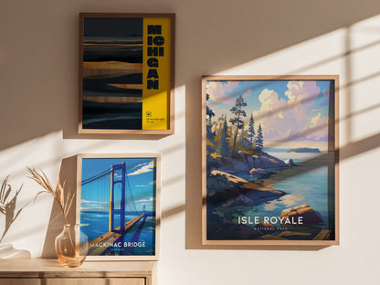 Three framed posters are displayed on a sunlit wall, featuring Mackinac Bridge, Isle Royale National Park, and a Michigan landscape. A vase with dried plants sits on a wooden surface.