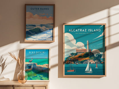 Framed wall art featuring Alcatraz Island, Outer Banks, and Fort Desoto posters displayed on a sunlit wall with a vase holding dried plants.