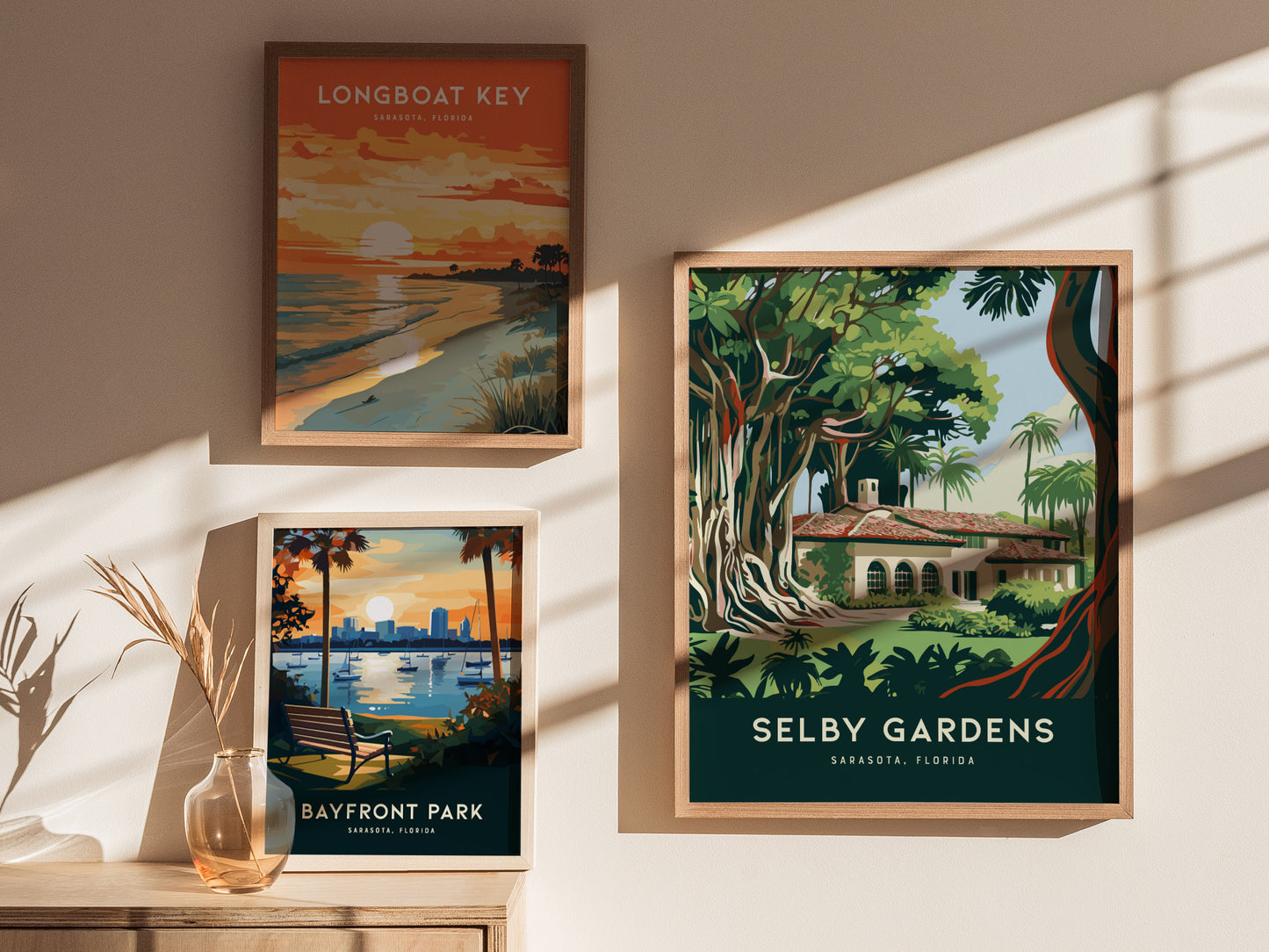Three framed posters hang on a wall, featuring vibrant landscapes of Longboat Key, Bayfront Park, and Selby Gardens in Sarasota, Florida, all illuminated by soft sunlight.