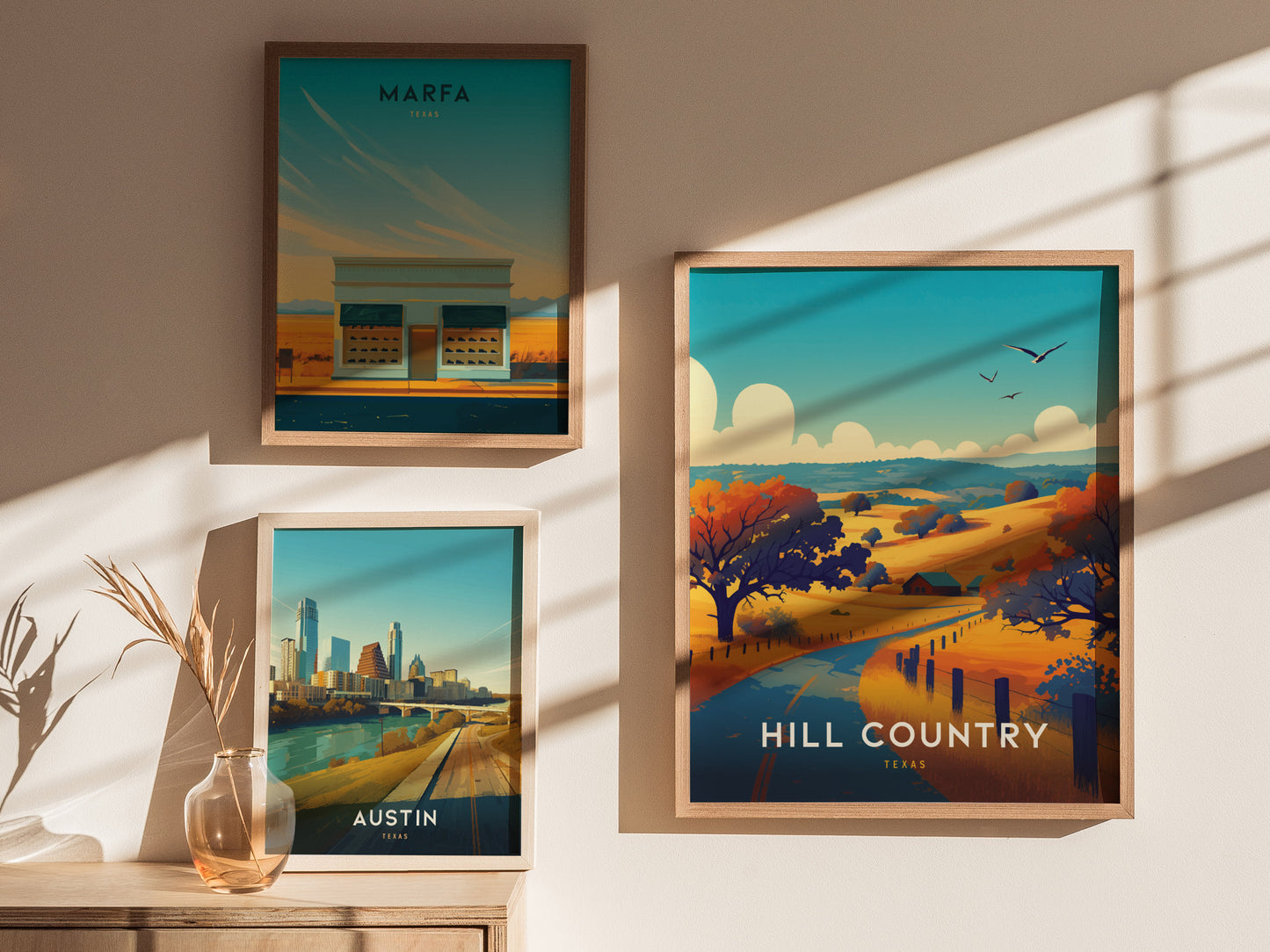 Three framed posters hang on a wall, showcasing scenic views of Marfa, Austin, and Hill Country in Texas. Soft shadows and a vase with dried plants add warmth.