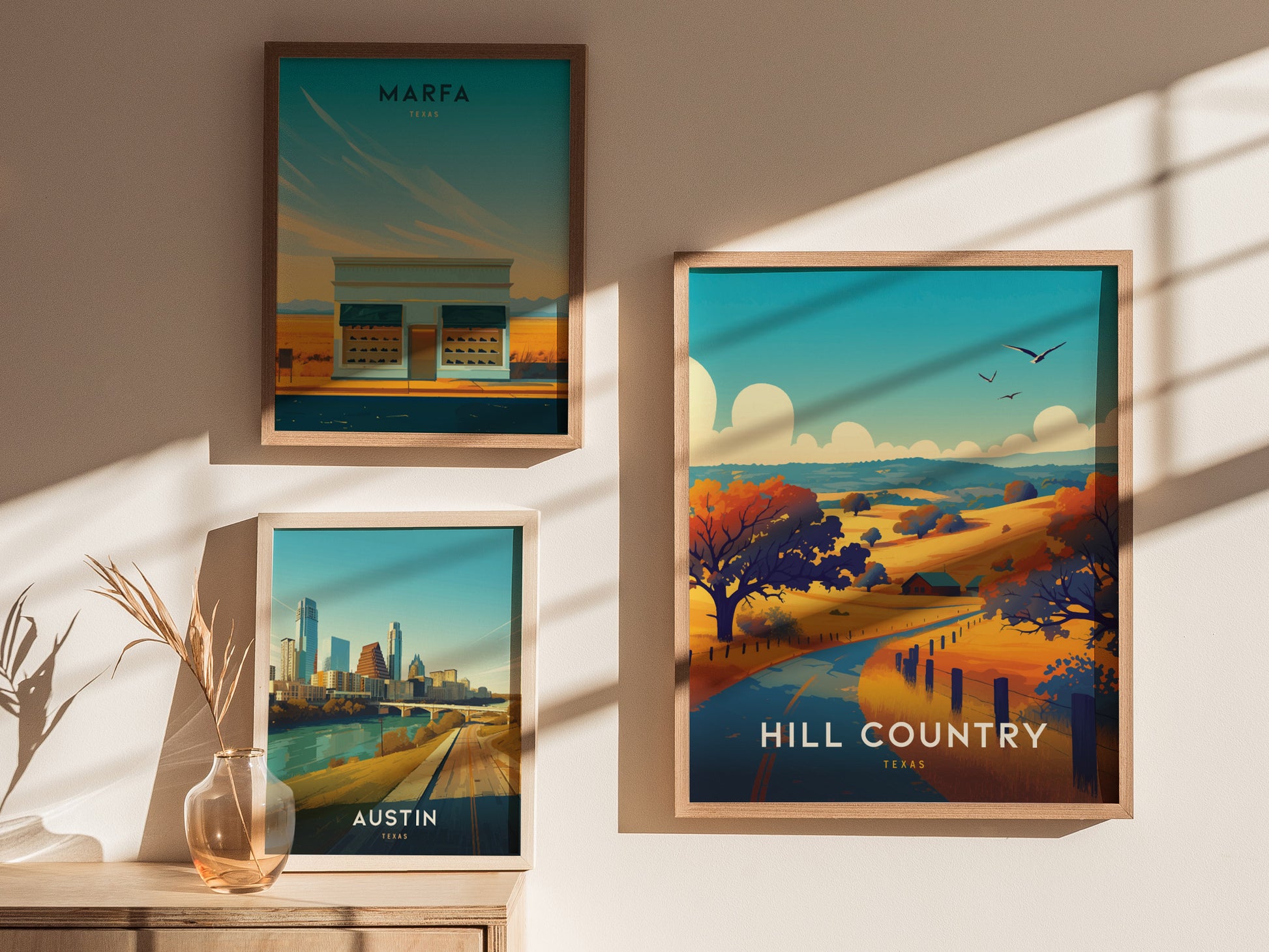 Three framed posters hang on a wall, showcasing scenic views of Marfa, Austin, and Hill Country in Texas. Soft shadows and a vase with dried plants add warmth.