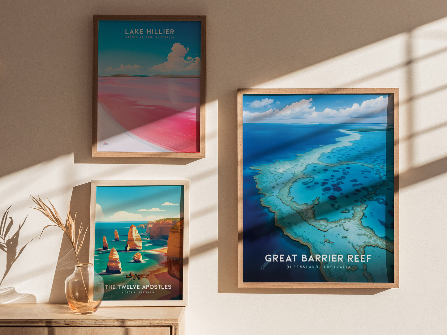 Three framed posters are displayed on a wall, depicting Lake Hillier, The Twelve Apostles, and the Great Barrier Reef, with natural lighting and a decorative vase nearby.