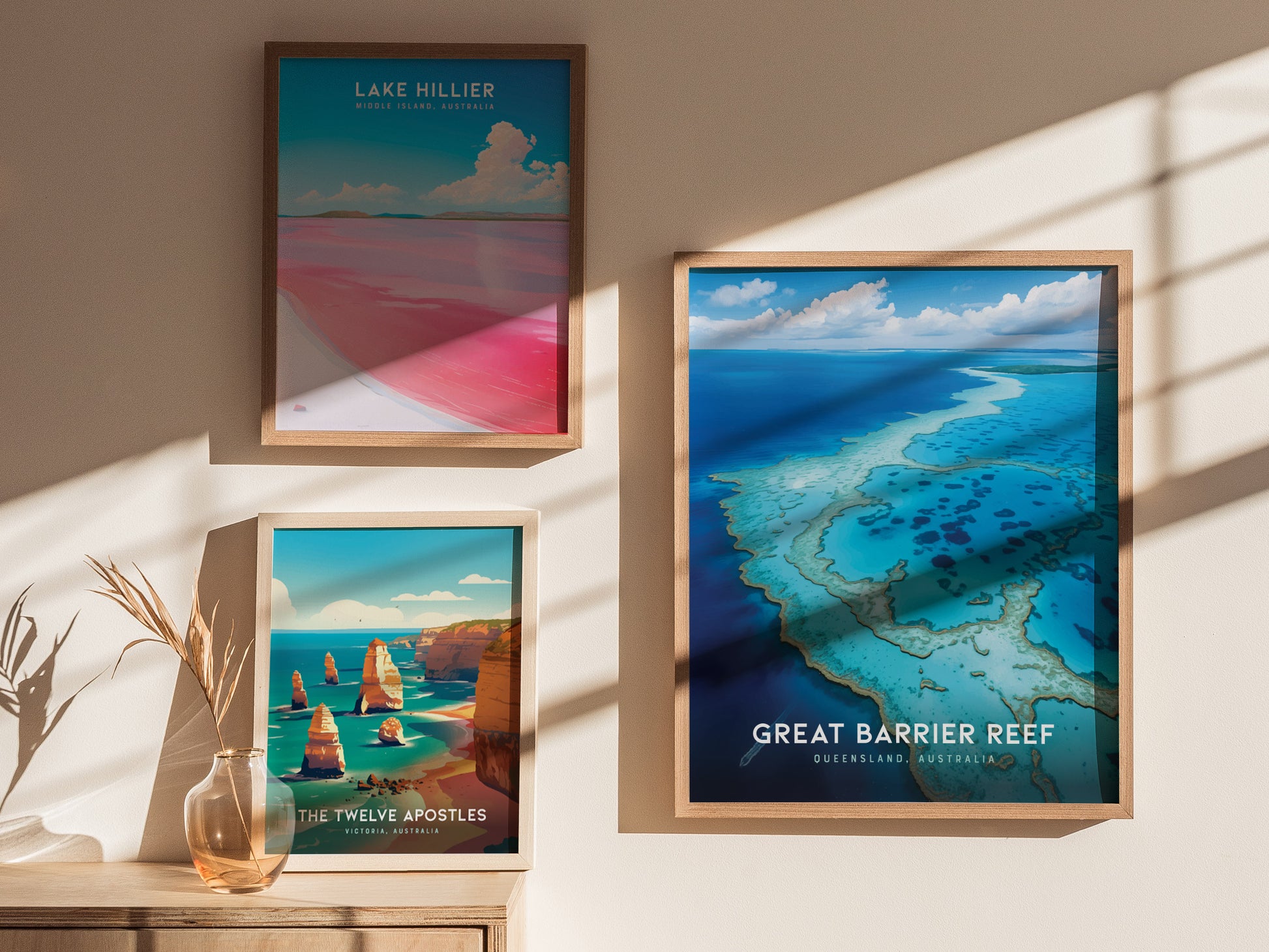 Three framed posters are displayed on a wall, depicting Lake Hillier, The Twelve Apostles, and the Great Barrier Reef, with natural lighting and a decorative vase nearby.