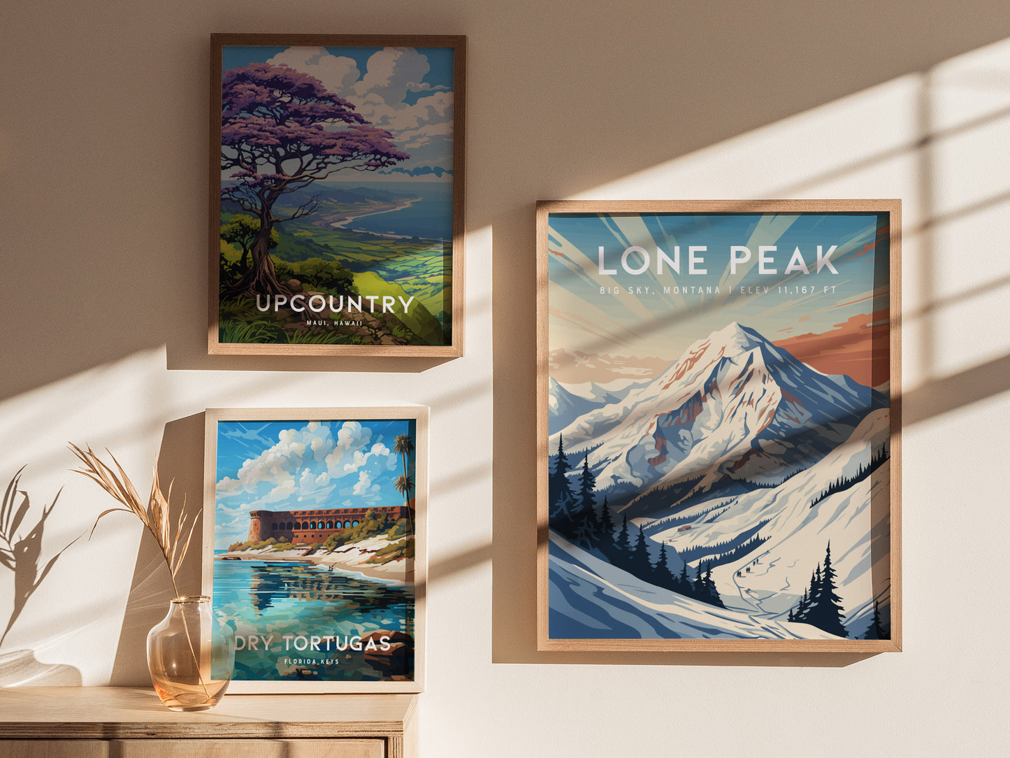 Three framed posters are displayed on a sunlit wall. The posters depict Lone Peak in Montana, a scenic view of Maui, Hawaii, and the Dry Tortugas in Florida Keys.