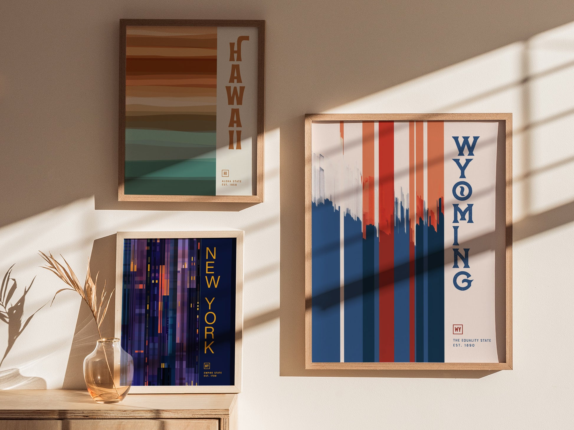 Three framed posters on a sunlit wall feature minimalist designs for Hawaii, Wyoming, and New York. Shadows from window panes add a dynamic touch to the scene.