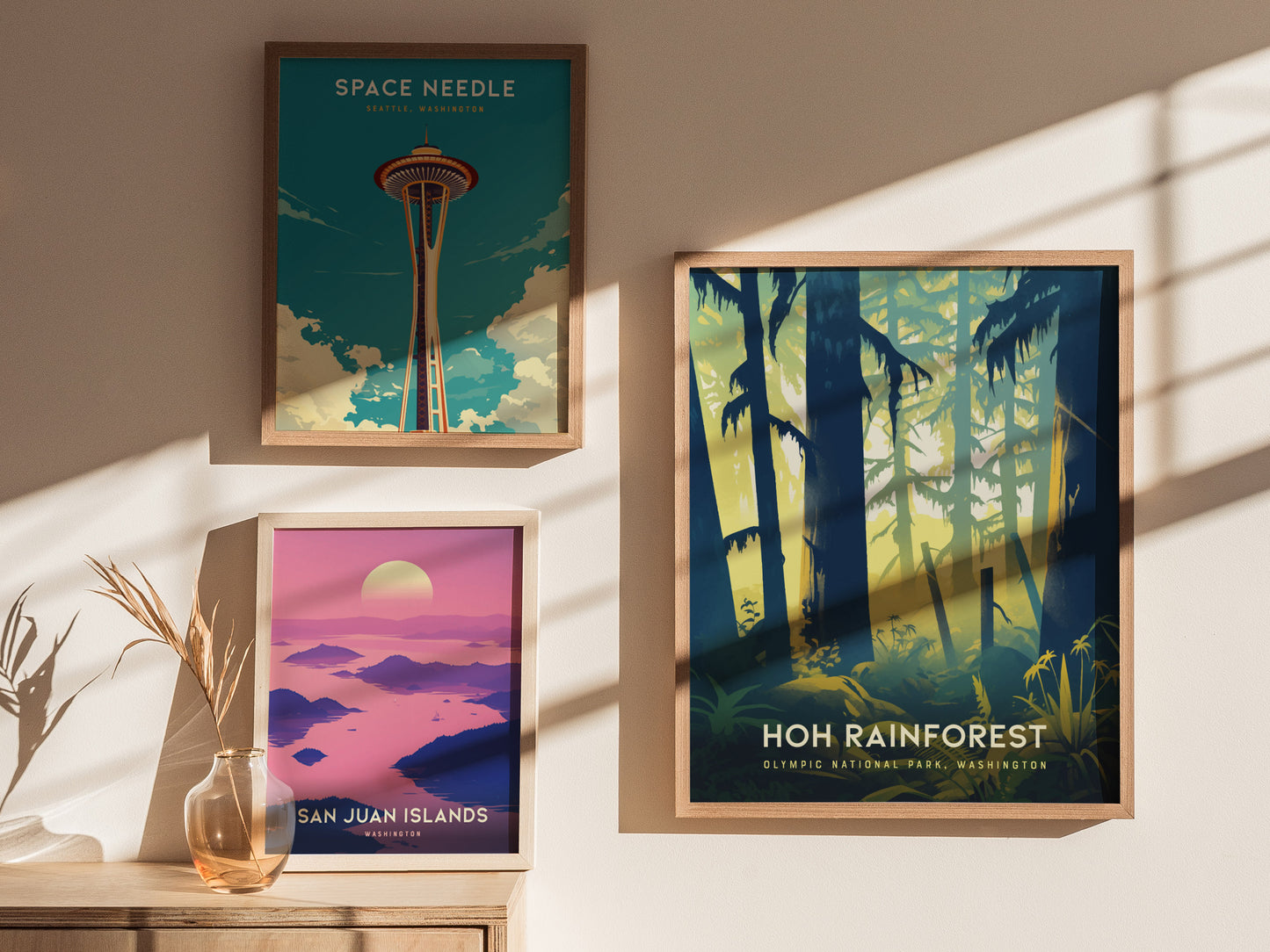 Three framed posters are displayed on a sunlit wall, featuring the Space Needle, San Juan Islands, and the Hoh Rainforest. A vase with dried plants sits nearby.