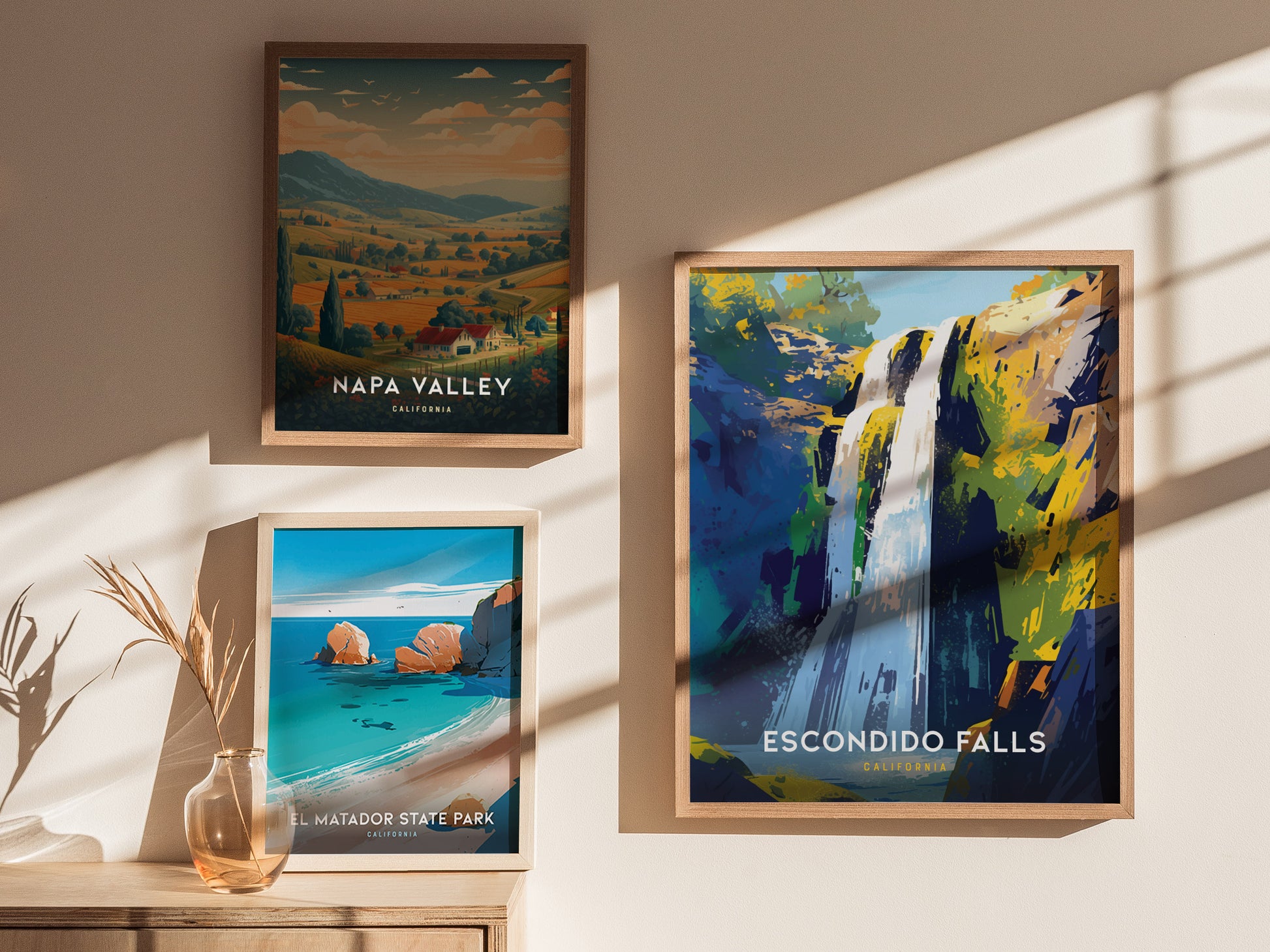 Framed posters of Napa Valley, El Matador State Park, and Escondido Falls are displayed on a wall, with natural sunlight casting soft shadows. A vase with dried plants sits nearby.