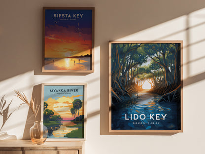 Three framed posters on a wall feature scenic illustrations of Siesta Key, Myakka River, and Lido Key in Sarasota, Florida. Sunlight casts shadows, enhancing the displays ambiance.