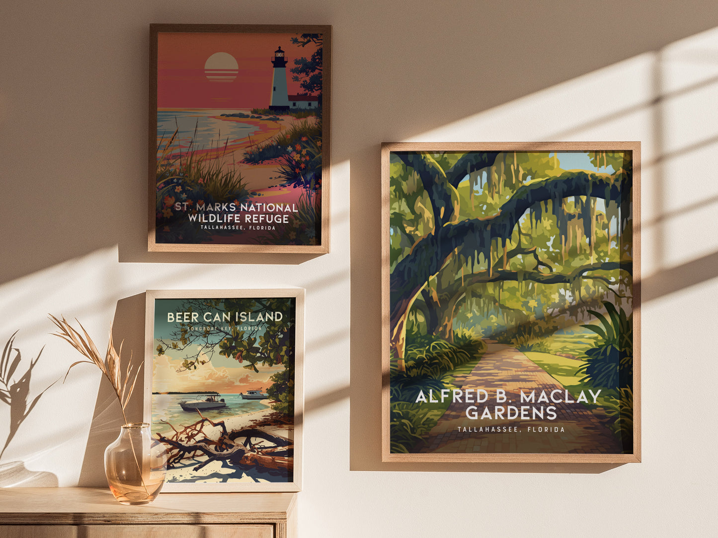 Framed posters on a wall depict St. Marks National Wildlife Refuge, Alfred B. Maclay Gardens, and Beer Can Island, with shadows and a vase with dried plants below.