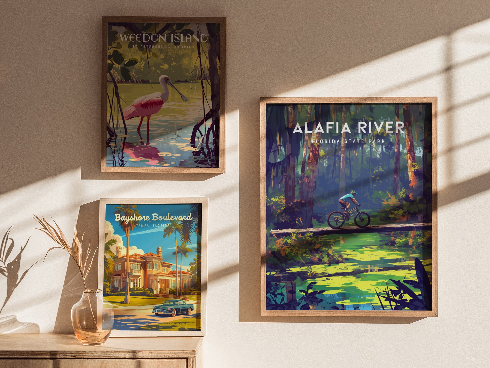 Three framed posters on a wall depict scenic Florida locations: a cyclist in a forest, a bird in wetlands, and a classic car by a mansion. Sunlight casts shadows.