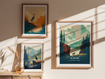 Framed posters of Glacier National Park, Everglades, and Great Smoky Mountains are displayed on a sunlit wall. A vase with dry branches sits on a wooden surface below.