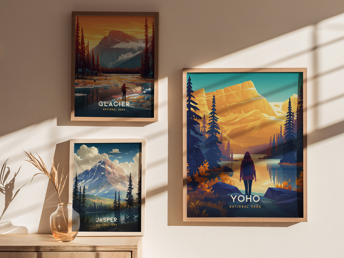 Three framed posters feature vibrant illustrations of national parks: Yoho, Glacier, and Jasper. Each showcases mountain landscapes with trees and figures, casting soft shadows on the wall.