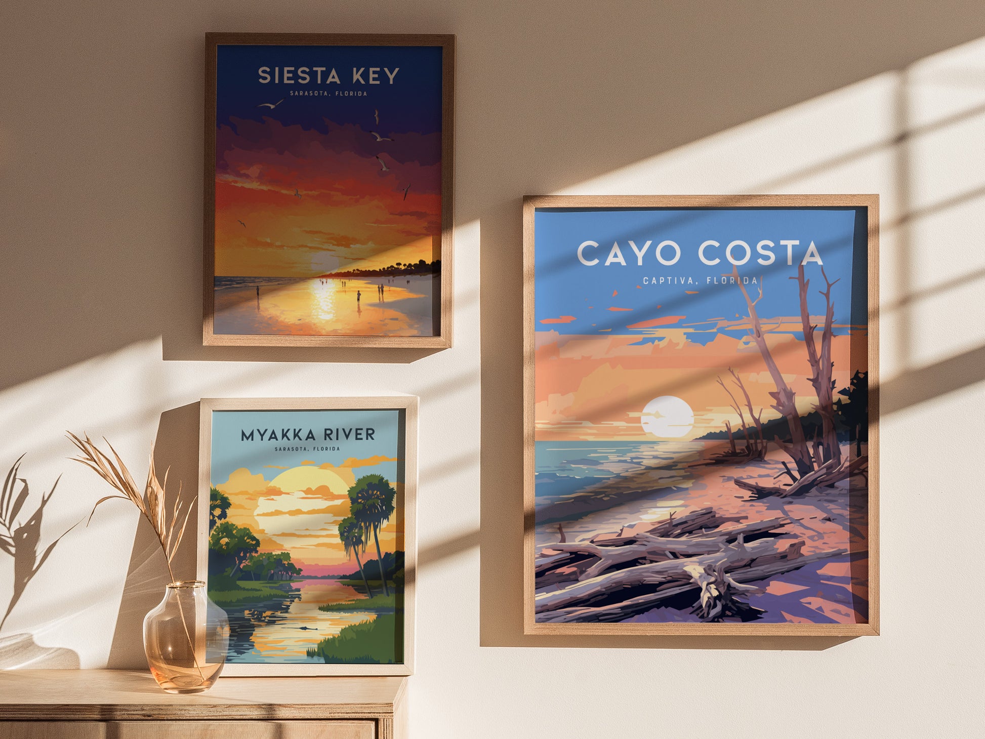 Three framed posters are displayed on a wall, depicting Siesta Key, Myakka River, and Cayo Costa, each featuring vibrant sunset scenes with landscapes and water.