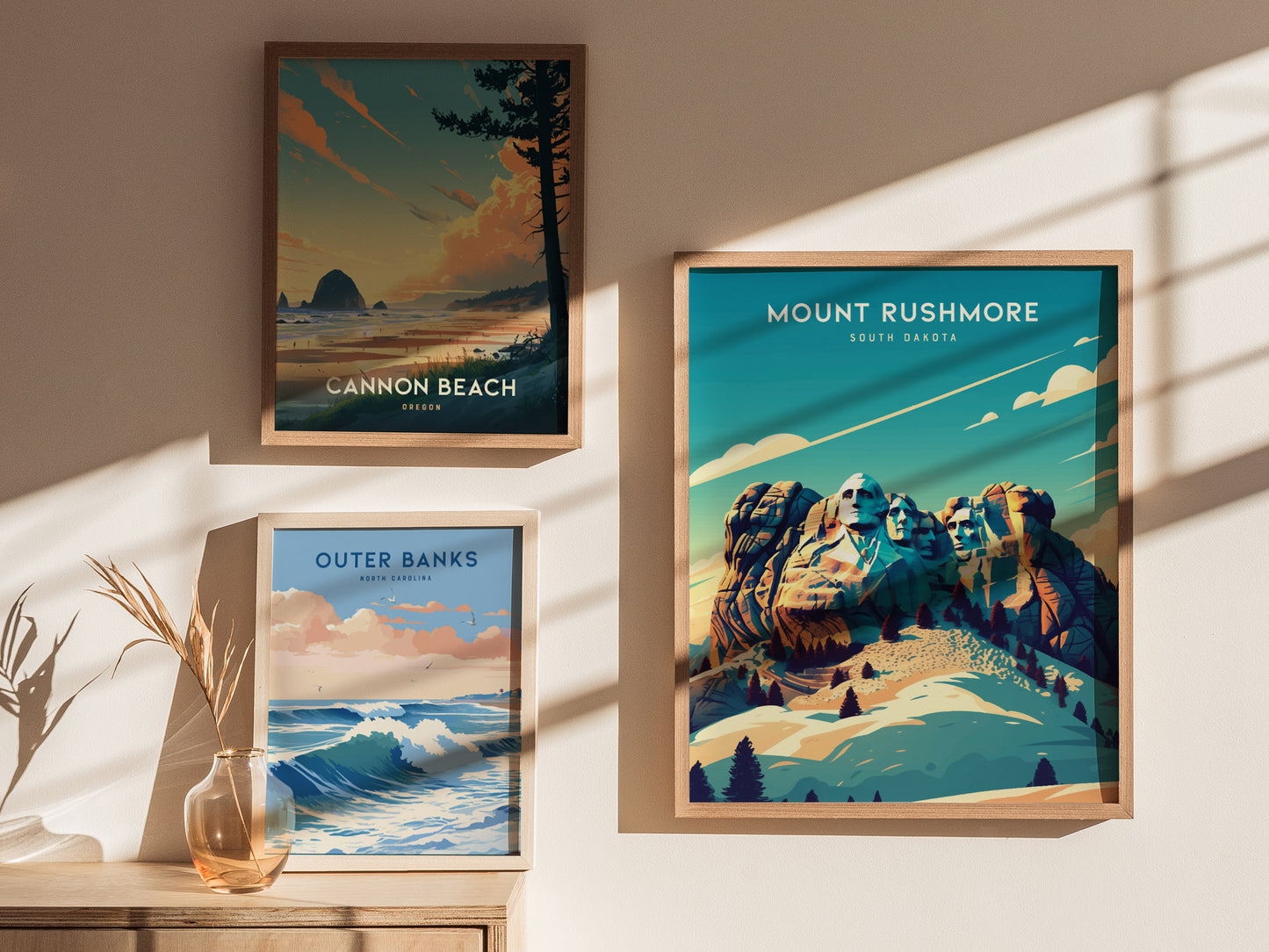 Three framed posters are displayed on a sunlit wall, featuring Cannon Beach, Outer Banks, and Mount Rushmore, each with vibrant landscapes and natural elements.