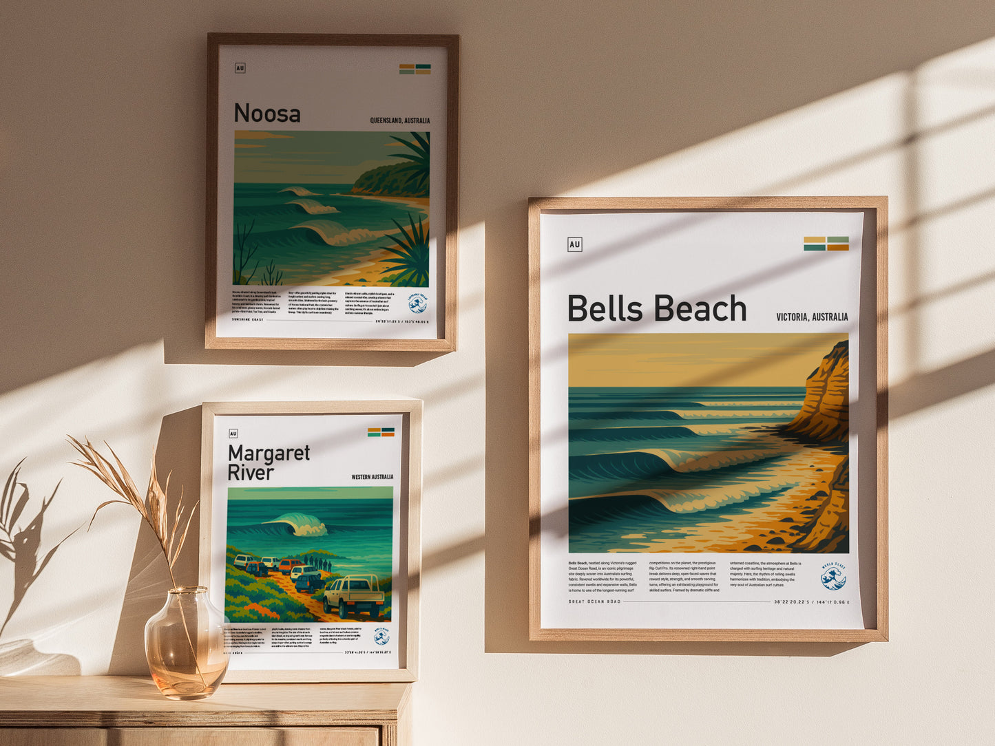 Framed posters featuring Bells Beach, Noosa, and Margaret River hang on a beige wall, with sunlight casting shadows. A small vase with dried plants is placed nearby.