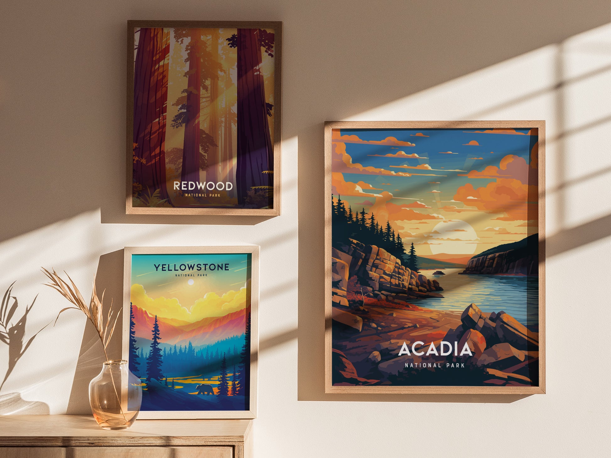 Three framed posters depicting national parks are displayed on a sunlit wall. The posters feature Acadia, Redwood, and Yellowstone, each with vibrant, colorful landscapes and bold lettering.