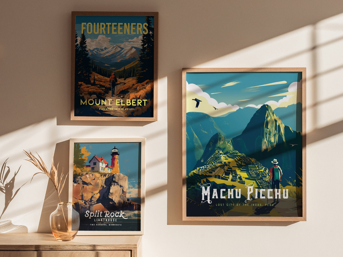 Three framed posters are displayed on a wall, depicting Mount Elbert, Split Rock Lighthouse, and Machu Picchu, with soft shadows and a decorative vase nearby.