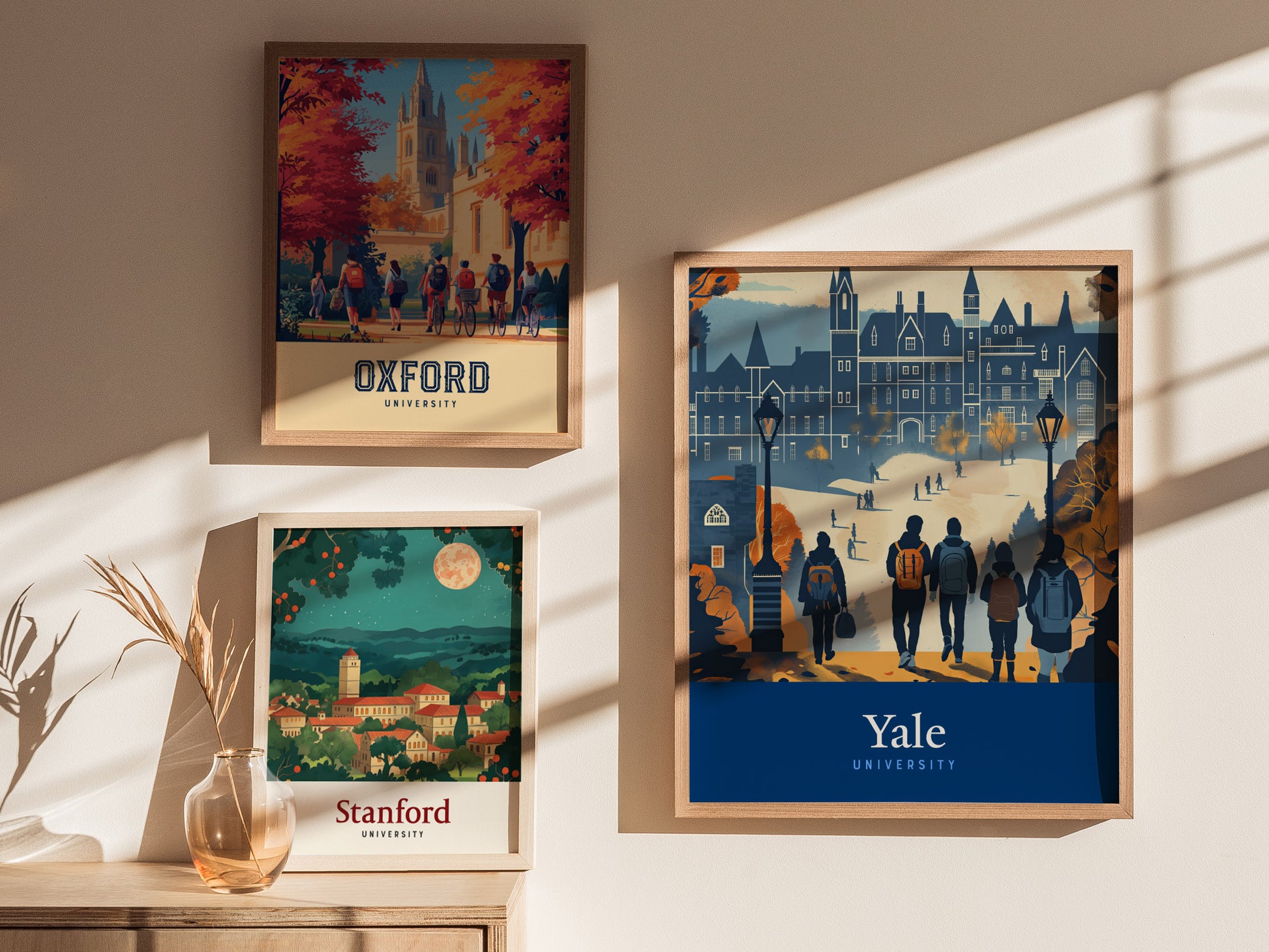 Three framed posters are displayed on a wall, featuring stylized illustrations of Oxford, Stanford, and Yale universities, with sunlight casting shadows across them.