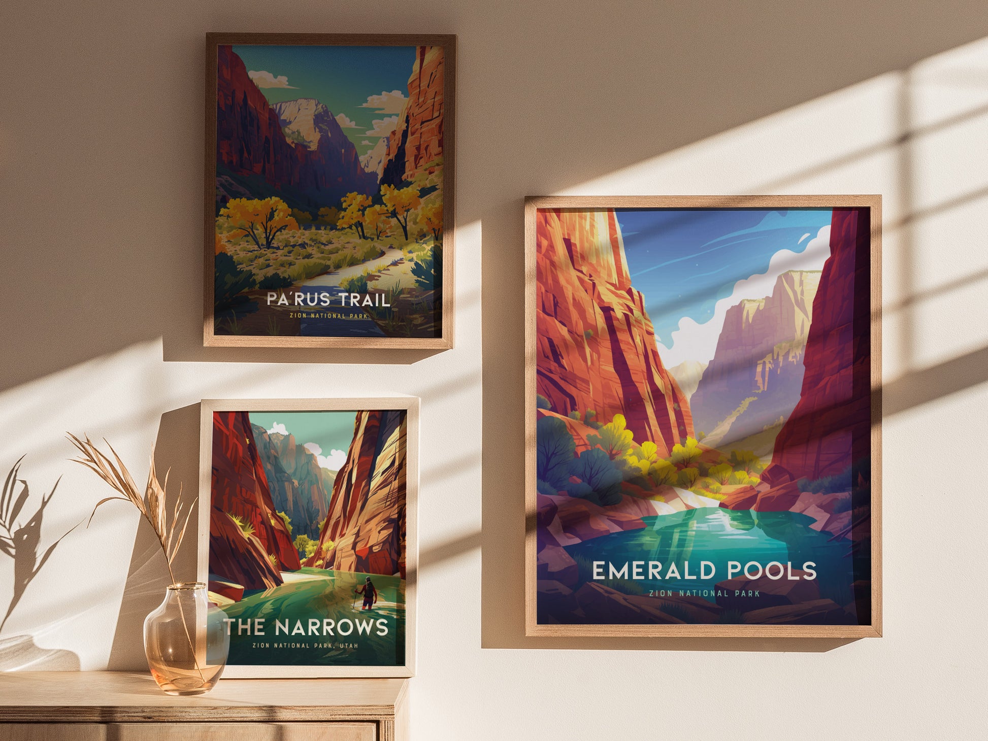 Three framed posters of Zion National Park landscapes are displayed on a sunlit wall. The posters depict Parus Trail, The Narrows, and Emerald Pools with vibrant, colorful illustrations.