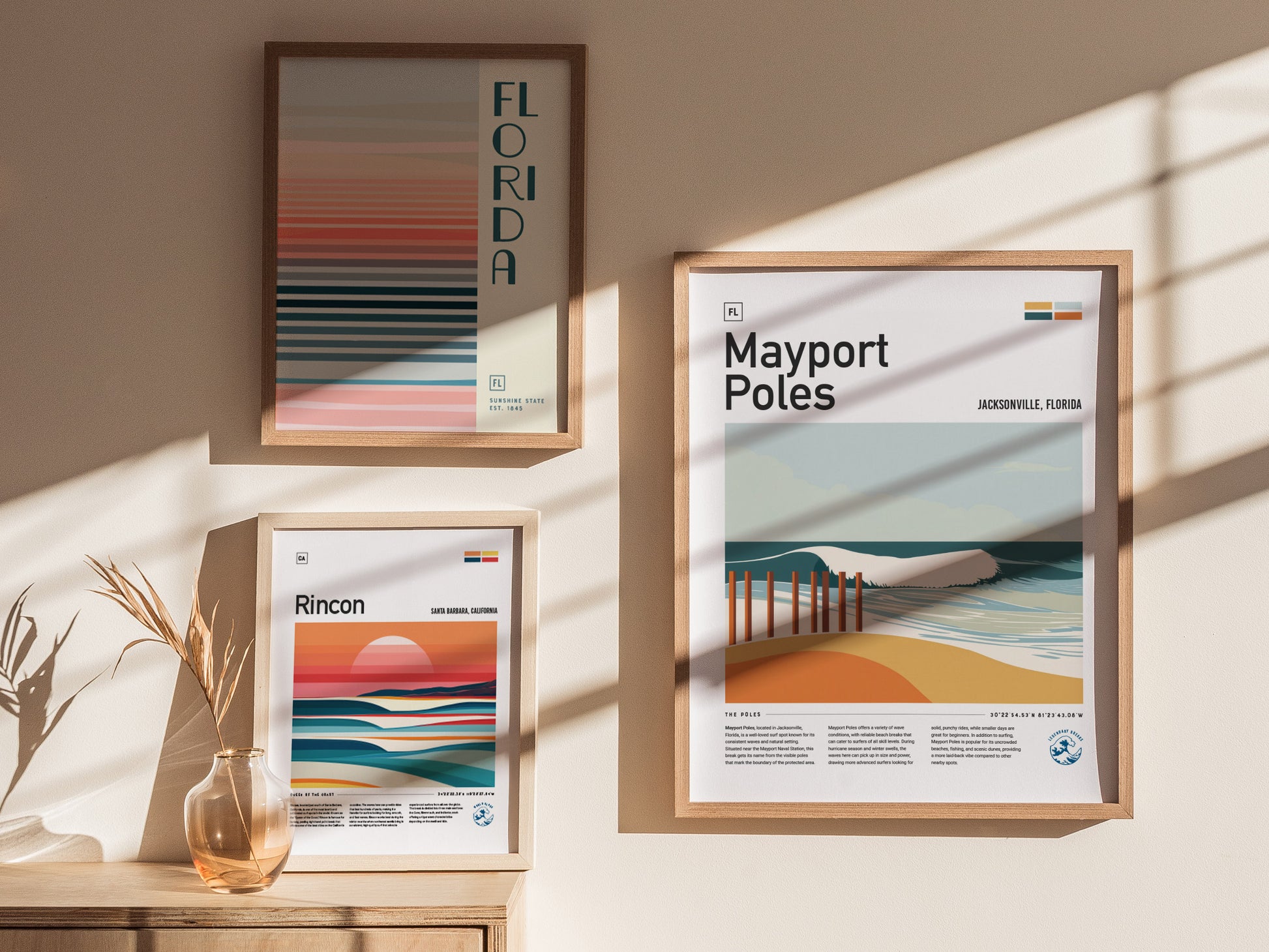 Three framed posters hang on a sunlit wall, featuring abstract designs of Florida, Mayport Poles in Jacksonville, and Rincon in Santa Barbara with coastal and wave imagery.