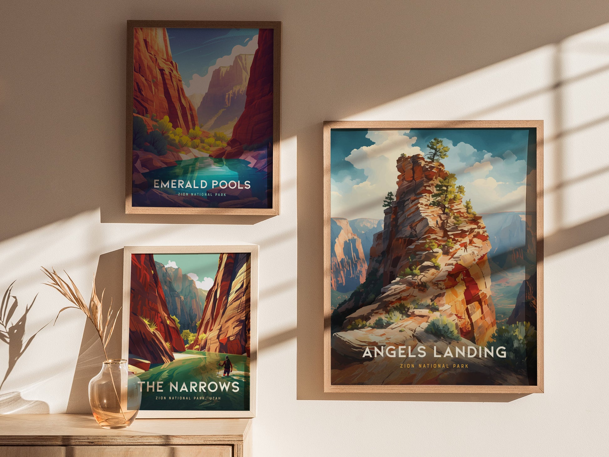Three framed posters depicting Zion National Park landscapes, including Angels Landing, Emerald Pools, and The Narrows, are displayed on a sunlit wall above a wooden surface with a vase.