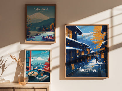 Framed posters on a wall depict Lake Ashi, Tokyo with Mount Fuji, and a snowy Takayama street scene. Sunlight casts shadows across the wall and a vase with dried grass.