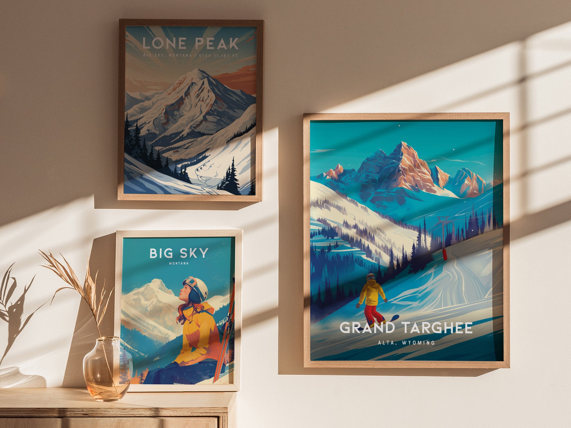 Three framed posters are displayed on a wall, depicting snowy mountain scenes from Lone Peak, Big Sky, and Grand Targhee, with sunlight casting shadows and a vase below.