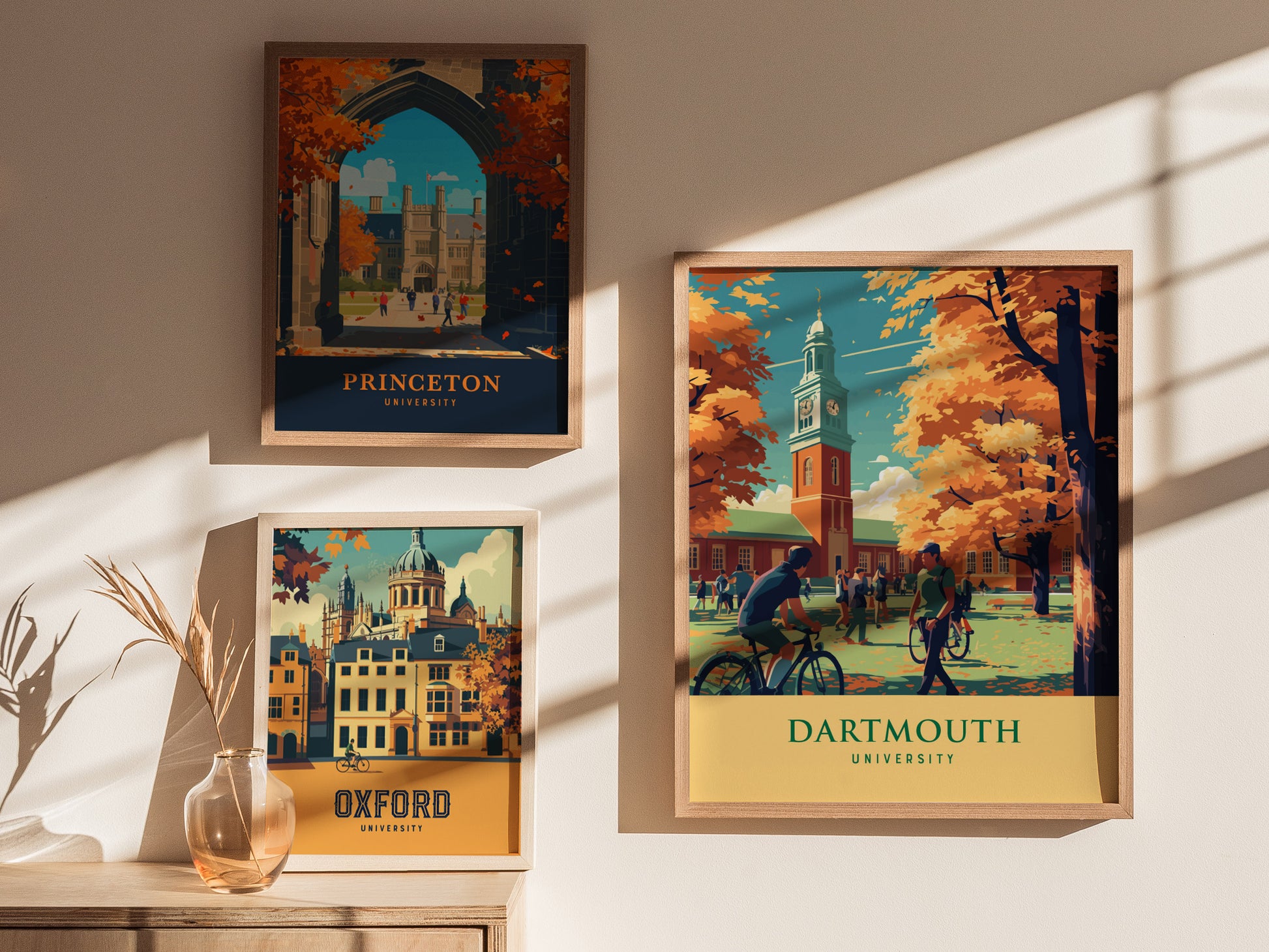 Framed posters of Princeton, Oxford, and Dartmouth University hang on a sunlit wall, with a vase of dried plants on a wooden table below.