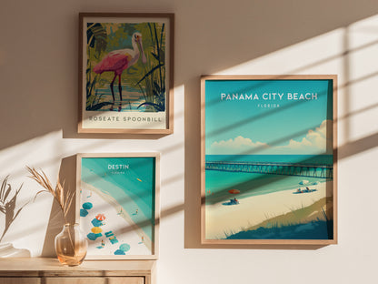 Three framed posters are displayed on a sunlit wall, featuring Panama City Beach, a roseate spoonbill, and Destin, Florida, with a vase and dried plant nearby.