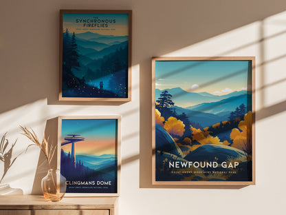 Three framed posters hang on a wall, each depicting scenic views of the Great Smoky Mountains. The Newfound Gap poster features vibrant blue and yellow tones with layered peaks and trees. Sunlight creates shadows on the wall.