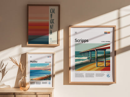 Three framed posters are displayed on a wall with soft shadows. They feature vibrant coastal themes of California, Malibu, and Scripps Pier, accompanied by a decorative vase with dried plants.