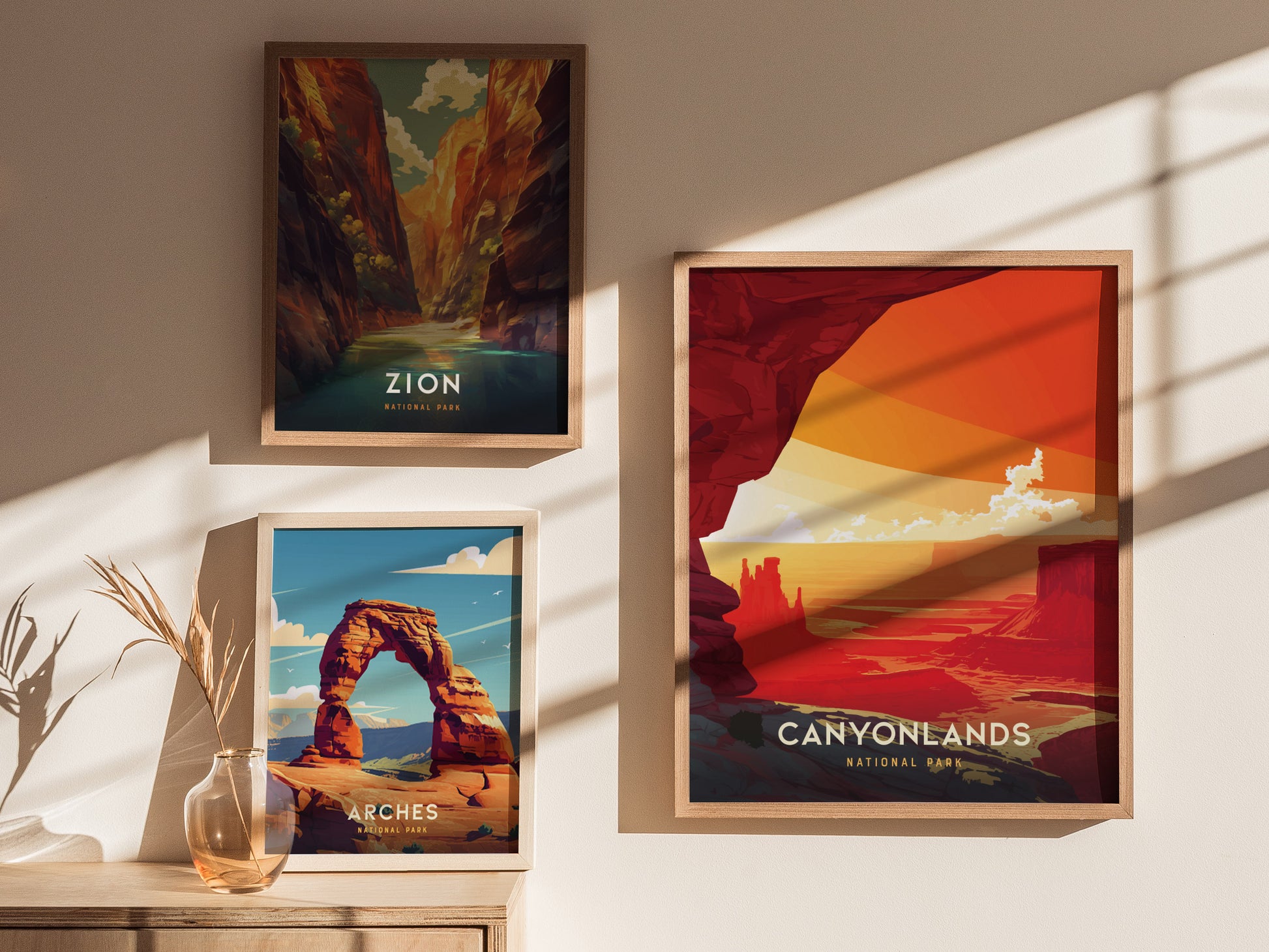 Three framed posters featuring Zion, Arches, and Canyonlands National Parks are displayed on a sunlit wall. A vase with dried plants sits on a wooden surface below.
