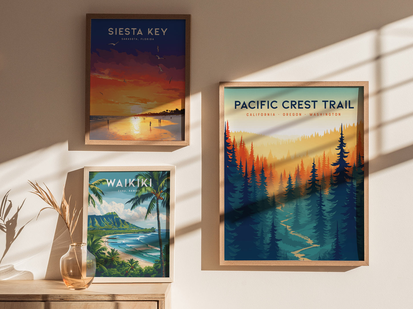 Three framed posters are displayed on a sunlit wall: Siesta Key with a beach sunset, Waikiki featuring a tropical coastline, and Pacific Crest Trail with a forest landscape.