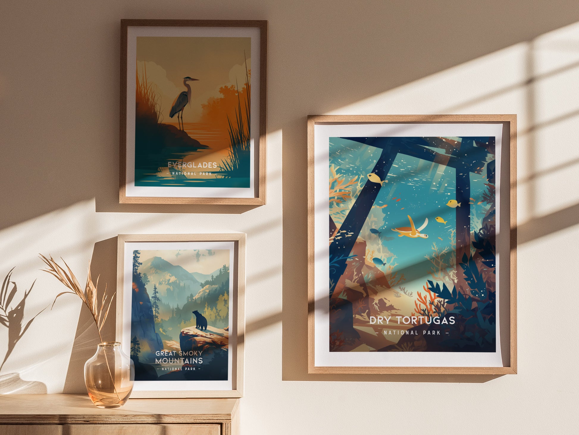 Three framed posters are displayed on a wall: Everglades with a heron, Great Smoky Mountains with a wolf, and Dry Tortugas with marine life. Sunlight creates shadows.